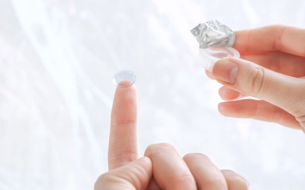 How Much Do Contact Lenses & Fittings Cost? 2 Gas permeable contact lenses being held by woman outside of photo edited